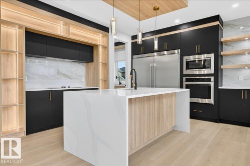 Kitchen featuring a waterfall island, integrated stainless steel appliances, black cabinetry with gold-toned hardware, natural wood-finish shelving, and a veined backsplash - 403 172 Avenue Nw, Edmonton, AB - Indoor Photo Showing Kitchen With Upgraded Kitchen