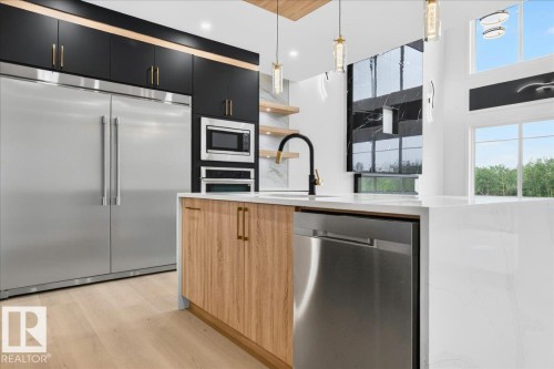 Contemporary kitchen featuring a large waterfall island with integrated stainless steel dishwasher, a black gooseneck faucet, and light wood-finish cabinetry - 403 172 Avenue Nw, Edmonton, AB - Indoor Photo Showing Kitchen With Upgraded Kitchen