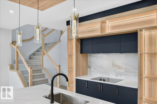 Modern kitchen featuring dark cabinetry, integrated cooktop, quartz countertops, and a white tile backsplash - 403 172 Avenue Nw, Edmonton, AB - Indoor Photo Showing Kitchen With Upgraded Kitchen
