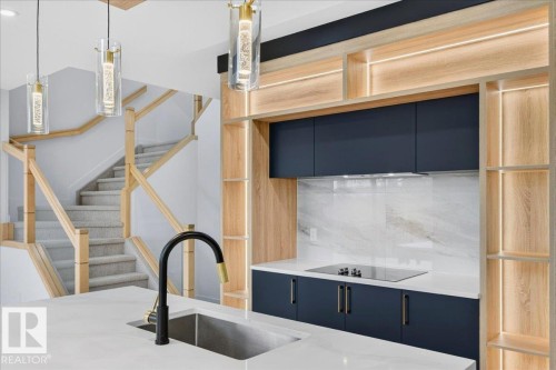 Contemporary kitchen featuring dark blue cabinetry, light wood-finish shelving with integrated lighting, a sleek cooktop, and a white countertop with a stainless steel sink - 403 172 Avenue Nw, Edmonton, AB - Indoor Photo Showing Kitchen With Upgraded Kitchen