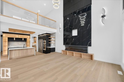 Open-concept living space featuring high ceilings, light wood-finish flooring, and a contemporary fireplace with a large-format black tile surround - 403 172 Avenue Nw, Edmonton, AB - Indoor