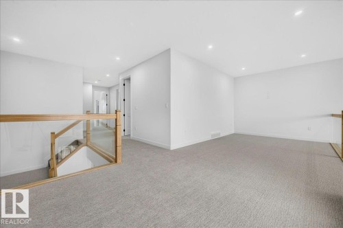 Open loft area featuring neutral-toned carpeting, recessed ceiling lighting, and a contemporary glass and wood-finish railing - 403 172 Avenue Nw, Edmonton, AB - Indoor Photo Showing Other Room