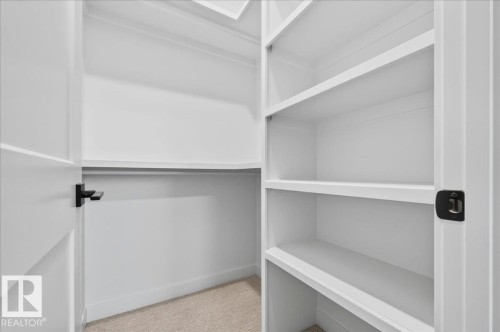 Walk-in closet featuring built-in shelving, hanging rod, neutral carpeting, and a crisp white color palette - 403 172 Avenue Nw, Edmonton, AB - Indoor With Storage