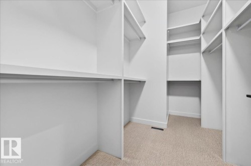 Walk-in closet featuring built-in shelving, multiple hanging rods, white trim, and light-toned carpeting - 403 172 Avenue Nw, Edmonton, AB - Indoor With Storage