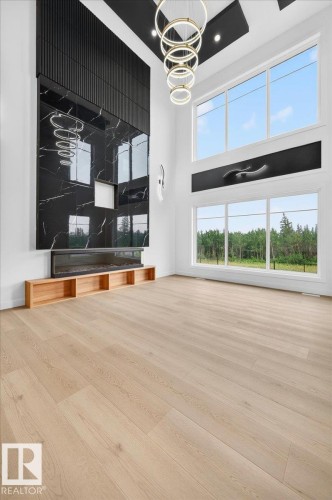 Open-concept living space featuring a floor-to-ceiling black marble-look fireplace surround, light wood-finish flooring, and a contemporary chandelier with stacked circular rings - 403 172 Avenue Nw, Edmonton, AB - Indoor Photo Showing Other Room