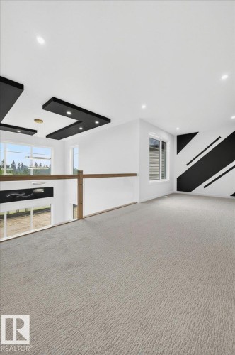 Loft area featuring light-toned carpeting, a modern glass railing with wood-finish top rail, recessed ceiling lighting, and a contemporary accent wall - 403 172 Avenue Nw, Edmonton, AB -  Photo Showing Other Room