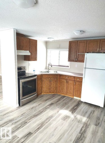 Kitchen featuring wood-finish cabinetry, light-toned countertops, a stainless steel electric range, and wood-finish flooring - 4819 51 Avenue, Millet, AB - Indoor Photo Showing Kitchen With Double Sink