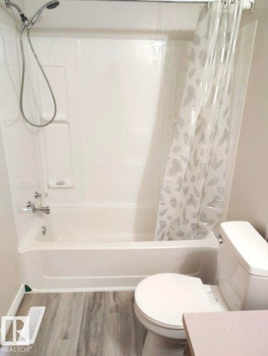 Bathroom featuring a white bathtub with an integrated shower, wood-finish flooring, and a white toilet - 4819 51 Avenue, Millet, AB - Indoor Photo Showing Bathroom