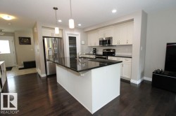 Kitchen featuring a central island with a dark countertop, white cabinetry, stainless steel appliances, and dark wood-finish flooring - 