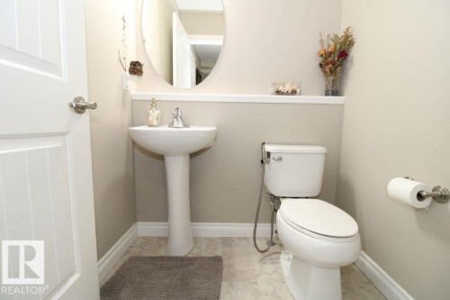 Pedestal sink with chrome faucet, oval mirror, and a wall-mounted toilet - 3048 Harvey Crescent Nw, Edmonton, AB - Indoor Photo Showing Bathroom