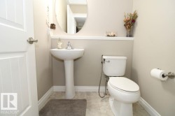 Pedestal sink with chrome faucet, oval mirror, and a wall-mounted toilet - 