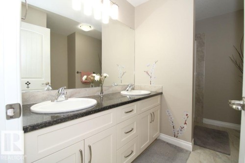Bathroom vanity featuring dual undermount sinks, a dark countertop, and a large mirror - 3048 Harvey Crescent Nw, Edmonton, AB - Indoor Photo Showing Bathroom
