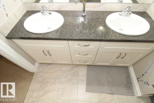 Dual vanity with cream cabinetry and a dark stone countertop featuring two undermount sinks with chrome fixtures - 3048 Harvey Crescent Nw, Edmonton, AB - Indoor Photo Showing Bathroom