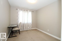 Neutral-toned bedroom featuring wall-to-wall carpeting, a window with curtain rod and sheer white drapes, baseboard trim, and a ceiling-mounted light fixture - 