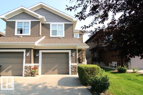Exterior featuring horizontal siding, stacked stone accents, two attached garages with overhead doors, and white-framed windows - 3048 Harvey Crescent Nw, Edmonton, AB - Outdoor With Facade