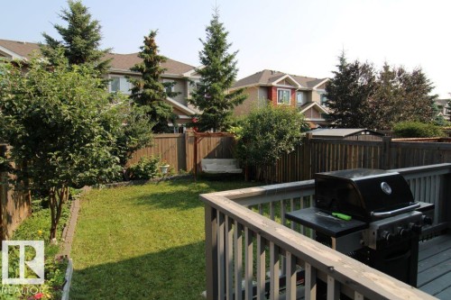 Spacious backyard featuring a wooden deck with railing, a green lawn area, mature trees, wood privacy fencing, and a built-in garden bed - 3048 Harvey Crescent Nw, Edmonton, AB - Outdoor