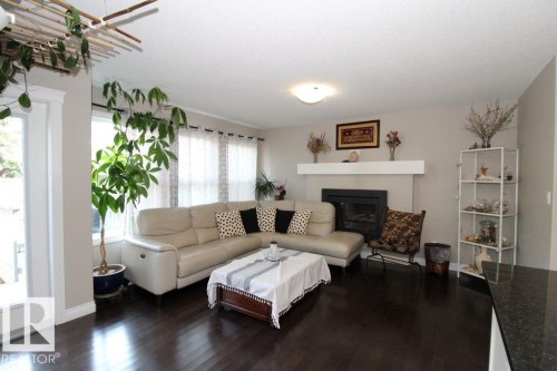 Spacious living area showcasing a neutral-toned sectional sofa, dark wood-finish flooring, and a built-in fireplace with white surround and mantel - 3048 Harvey Crescent Nw, Edmonton, AB - Indoor Photo Showing Living Room With Fireplace