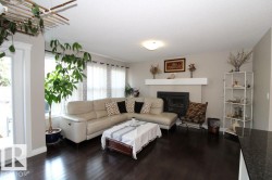 Spacious living area showcasing a neutral-toned sectional sofa, dark wood-finish flooring, and a built-in fireplace with white surround and mantel - 
