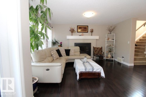 Living area with dark wood-finish flooring, a contemporary fireplace with a white mantel, neutral wall paint, and a staircase featuring carpeted treads and a wood handrail - 3048 Harvey Crescent Nw, Edmonton, AB - Indoor Photo Showing Living Room With Fireplace