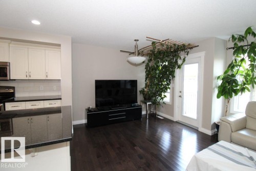 Spacious living area featuring dark wood-finish flooring, a contemporary ceiling light fixture, and a white paneled door with glass insert - 3048 Harvey Crescent Nw, Edmonton, AB - Indoor