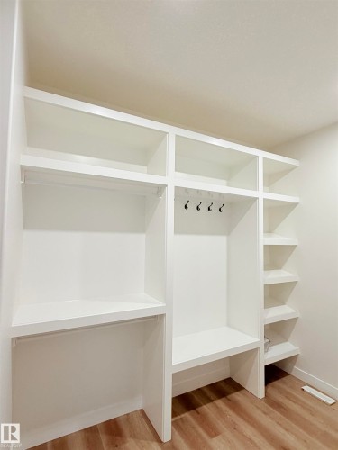 Built-in closet system featuring white shelving, hanging rods, an integrated bench, and black coat hooks - 3150 Magpie Way Nw, Edmonton, AB - Indoor With Storage
