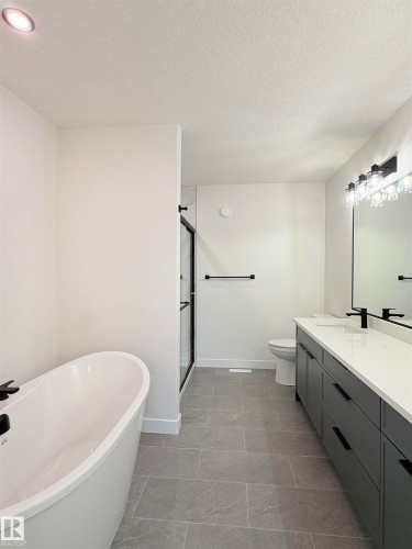 Modern bathroom featuring a freestanding soaking tub with matte black fixtures, a glass-enclosed shower with a black frame, and a dual-sink vanity with dark cabinetry and a light-colored countertop - 3150 Magpie Way Nw, Edmonton, AB - Indoor Photo Showing Bathroom