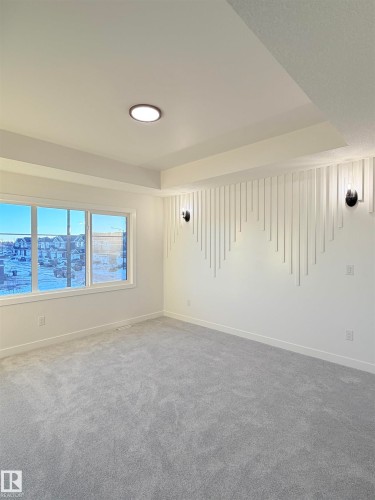 Spacious room featuring light gray carpeting, a textured accent wall with decorative vertical panels, and two wall-mounted sconces - 3150 Magpie Way Nw, Edmonton, AB - Indoor Photo Showing Other Room