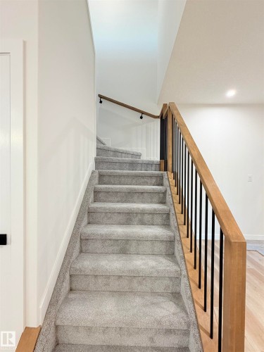 Carpeted staircase featuring a light wood railing with black metal balusters and a wall-mounted light wood handrail - 3150 Magpie Way Nw, Edmonton, AB - Indoor Photo Showing Other Room