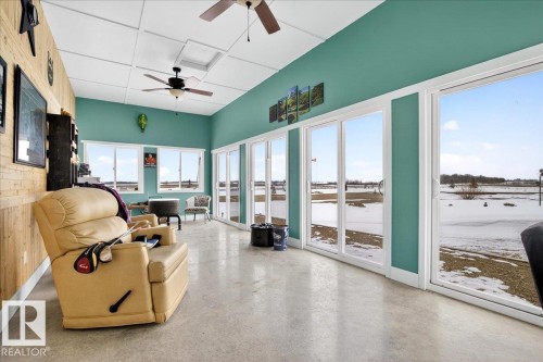 Expansive room featuring multiple sliding glass doors and windows offering abundant natural light, a wood-paneled accent wall, a vaulted ceiling with integrated lighting and ceiling fans, and durable flooring - 531064 Range Road 174, Rural Lamont County, AB - Indoor