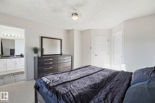 Carpeted bedroom featuring a ceiling fan, light-colored walls, and a convenient bathroom entry - 215 85 Street Sw, Edmonton, AB 