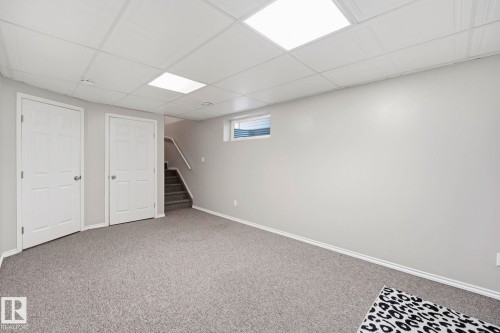 Spacious room featuring light gray walls, plush gray carpeting, and a white drop ceiling with recessed lighting - 215 85 Street Sw, Edmonton, AB 