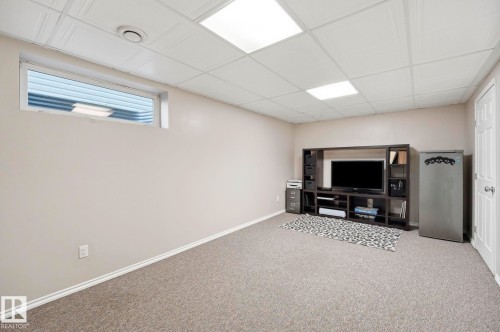 Carpeted recreation room featuring an egress window, drop ceiling with recessed lighting, and painted walls - 215 85 Street Sw, Edmonton, AB 
