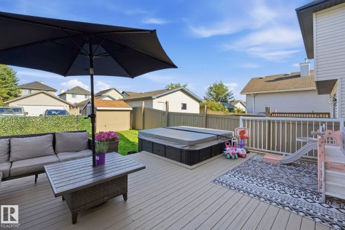 Spacious outdoor deck featuring a hot tub, white railings, and direct access to a fenced yard with a manicured lawn - 215 85 Street Sw, Edmonton, AB 