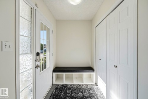 Entryway featuring a white paneled door with glass inserts, a built-in storage bench, and bi-fold closet doors - 215 85 Street Sw, Edmonton, AB 