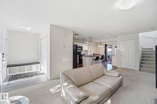 Open-concept living space featuring neutral carpet flooring, a light-filled interior with recessed ceiling lighting, and seamless sightlines to the kitchen area - 215 85 Street Sw, Edmonton, AB 