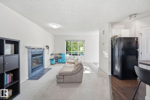 Open-concept living space featuring a tiled fireplace with mantel, light-toned carpeting, and a window with natural light - 215 85 Street Sw, Edmonton, AB 