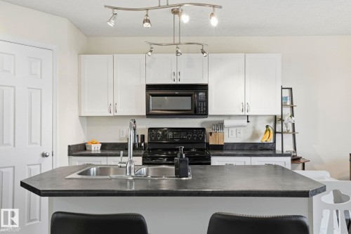 Kitchen featuring an island with a double basin sink, white cabinetry, and contrasting dark countertops - 215 85 Street Sw, Edmonton, AB 
