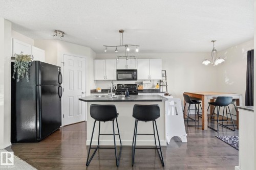 Open-concept kitchen with dark wood-finish flooring, white cabinetry, and black appliances - 215 85 Street Sw, Edmonton, AB 