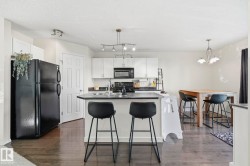 Open-concept kitchen with dark wood-finish flooring, white cabinetry, and black appliances - 