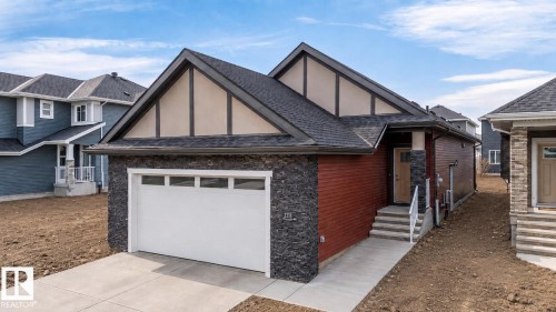 Contemporary single-story residence featuring a dark shingle roof, stone facade accents, red horizontal siding, an attached garage with a white door, and a concrete driveway - 3318 Chickadee Drive Nw, Edmonton, AB - Outdoor
