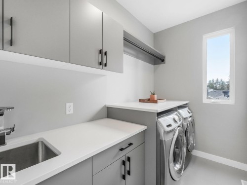 Dedicated laundry area featuring gray cabinetry with black hardware, white countertops, stainless steel sink, and a window for natural light - 11613 72 Avenue Nw, Edmonton, AB - Indoor Photo Showing Laundry Room