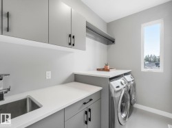 Dedicated laundry area featuring gray cabinetry with black hardware, white countertops, stainless steel sink, and a window for natural light - 