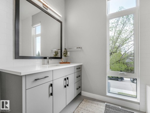 Modern bathroom featuring a tall window, a light gray vanity with black hardware, a white countertop, and a large black-framed mirror with integrated lighting - 11613 72 Avenue Nw, Edmonton, AB - Indoor Photo Showing Bathroom