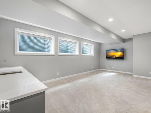 Spacious room with light gray walls, plush carpeting, three egress windows, a built-in entertainment area, and recessed lighting - 11613 72 Avenue Nw, Edmonton, AB - Indoor