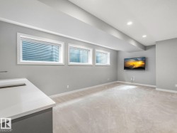 Spacious room with light gray walls, plush carpeting, three egress windows, a built-in entertainment area, and recessed lighting - 