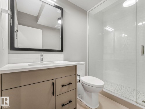 Contemporary bathroom featuring a neutral-toned vanity with black hardware, a rectangular undermount sink, and a framed mirror with integrated lighting - 11613 72 Avenue Nw, Edmonton, AB - Indoor Photo Showing Bathroom