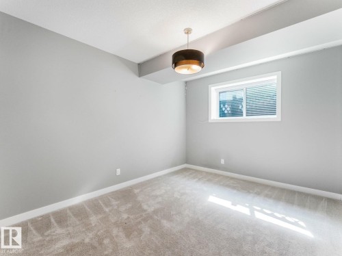 Room featuring light gray walls, plush carpeting, a modern drum pendant light fixture, a white-framed window with horizontal blinds, and white baseboards - 11613 72 Avenue Nw, Edmonton, AB - Indoor Photo Showing Other Room