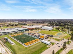 Aerial perspective showcasing a large sports complex featuring a prominent football field with stadium seating, multiple athletic tracks, a baseball diamond, and an inflatable dome structure - 