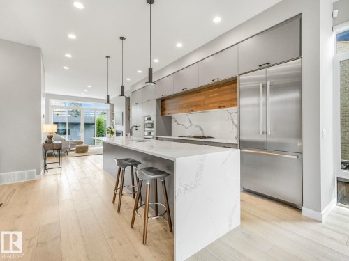 Open-concept kitchen featuring a waterfall island with a stone countertop, integrated stainless steel appliances, wood-finish flooring, and recessed lighting - 11613 72 Avenue Nw, Edmonton, AB - Indoor Photo Showing Kitchen With Upgraded Kitchen