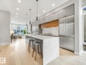 Open-concept kitchen featuring a waterfall island with a stone countertop, integrated stainless steel appliances, wood-finish flooring, and recessed lighting - 11613 72 Avenue Nw, Edmonton, AB  - Indoor Photo Showing Kitchen With Upgraded Kitchen 